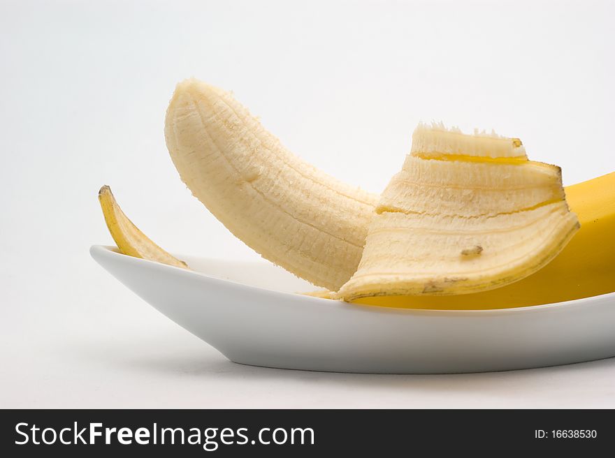 Half-cleared banana on a plate on a white background closeup