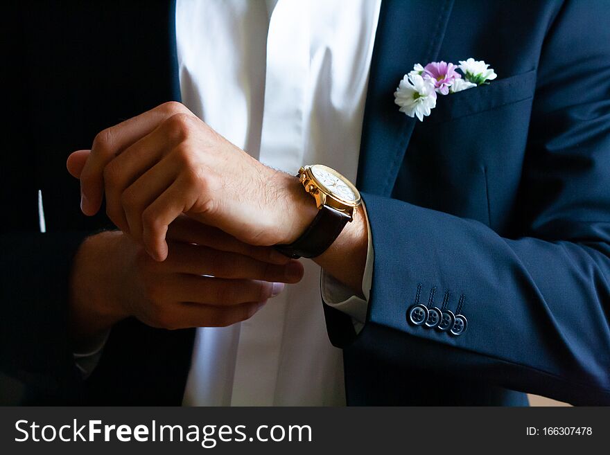 Closeup on the hands of the groom or groomsman putting on or adjusting a watch on the day of the wedding celebration, with a navy blue blazer and crisp white shirt, checking the time, getting ready, dressing up. Closeup on the hands of the groom or groomsman putting on or adjusting a watch on the day of the wedding celebration, with a navy blue blazer and crisp white shirt, checking the time, getting ready, dressing up