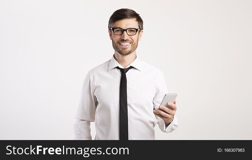 Business App. Smiling Man Using Mobile Phone Looking At Camera Standing Over White Studio Background. Panorama, Empty Space. Business App. Smiling Man Using Mobile Phone Looking At Camera Standing Over White Studio Background. Panorama, Empty Space