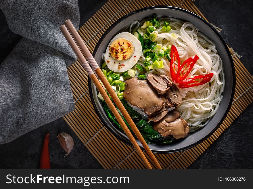 Chinese noodles with chicken giblets with an egg, green onions with lying chopsticks in a bowl