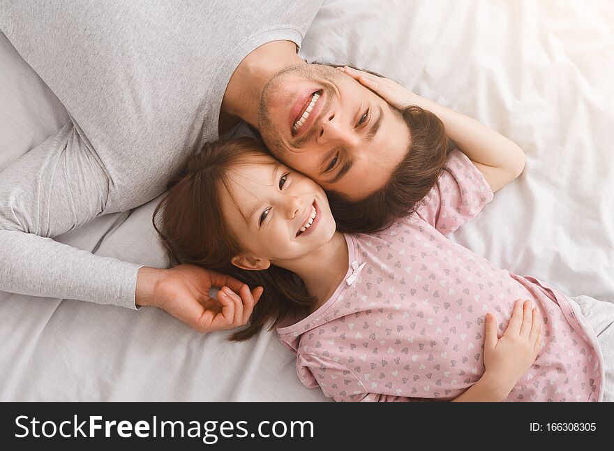 Top view of handsome young father and his cute little daughter looking at camera and smiling, lying on bed at home, just woke up, affectionate concept. Top view of handsome young father and his cute little daughter looking at camera and smiling, lying on bed at home, just woke up, affectionate concept