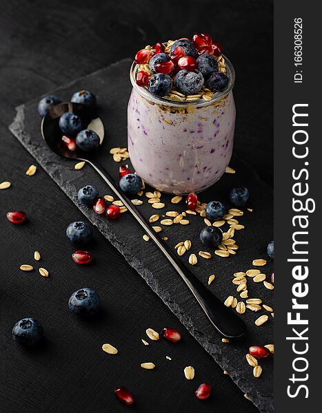 Healthy breakfast concept. Jars of homemade yogurt with blueberries, pomegranate seeds and oats on black background. Vertical