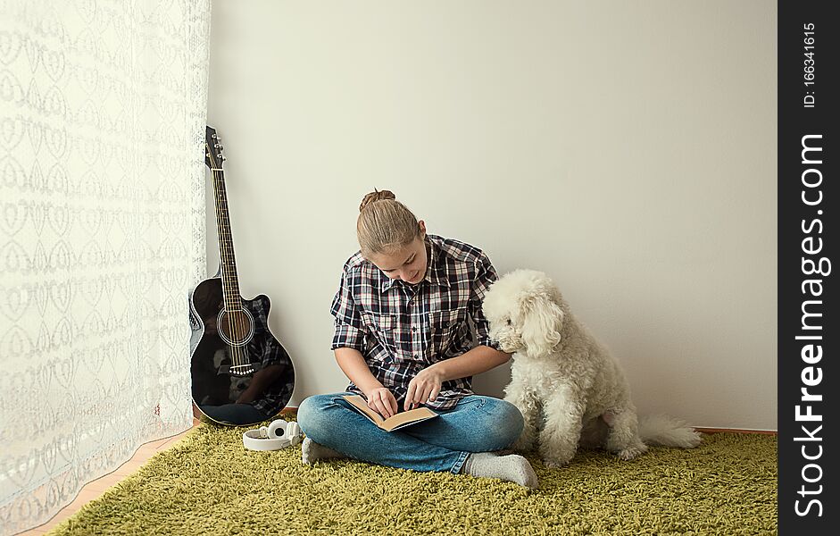 Teenager on the carpet by the window reading a book in the company of the dog. Teenager on the carpet by the window reading a book in the company of the dog