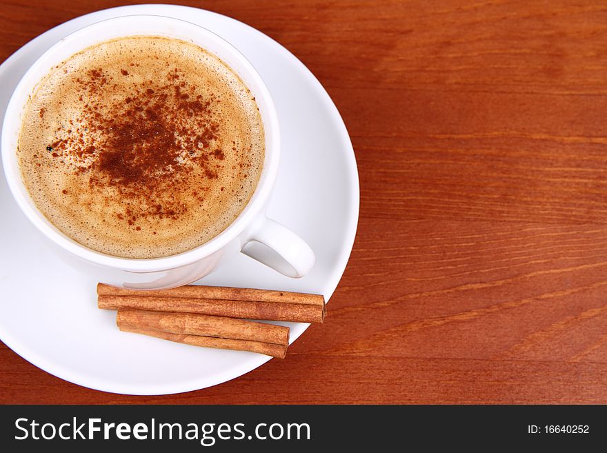 Cup of coffee sprinkled with cinnamon and with cinnamon sticks on wooden background. Cup of coffee sprinkled with cinnamon and with cinnamon sticks on wooden background