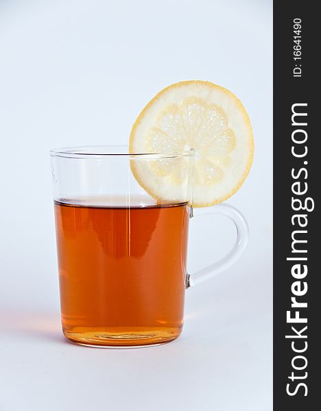 Glass of hot black tea with lemon and a tea pot