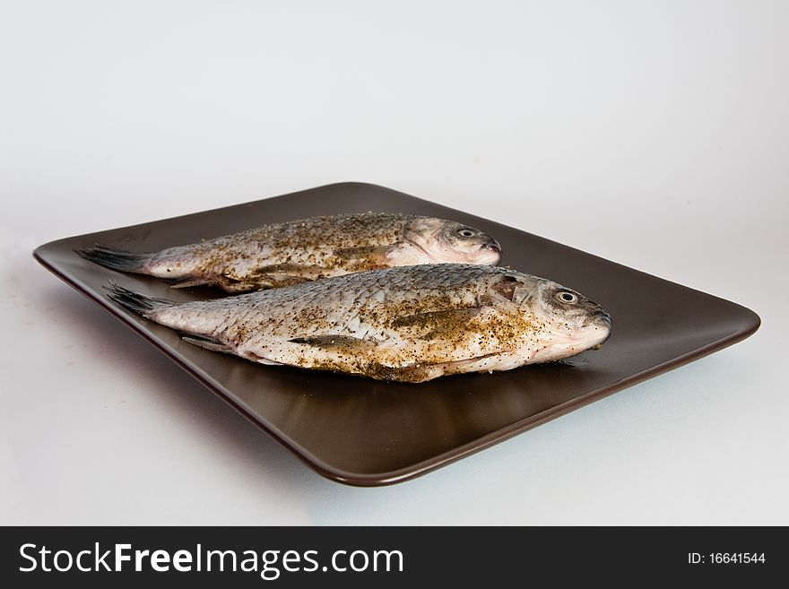 Pair of raw fresh crucian , spiced, on a brown plate
