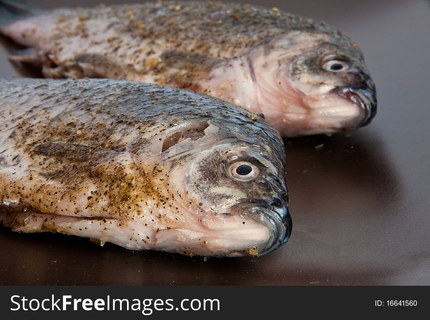 Pair of raw fresh crucian , spiced, on a brown plate