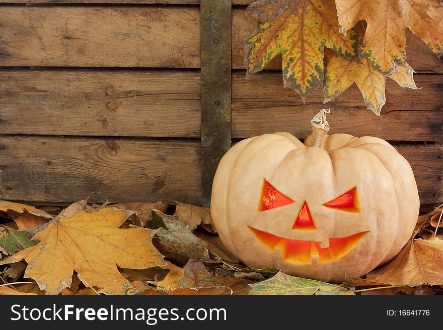 Creepy carved pumpkin face on wooden bacground and autumn leafs. Creepy carved pumpkin face on wooden bacground and autumn leafs