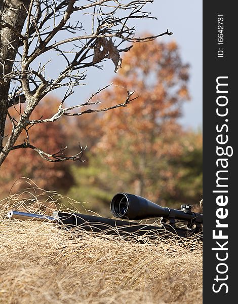 Sniper laying on the ground covered in a ghille suite tall grass and trees in the background