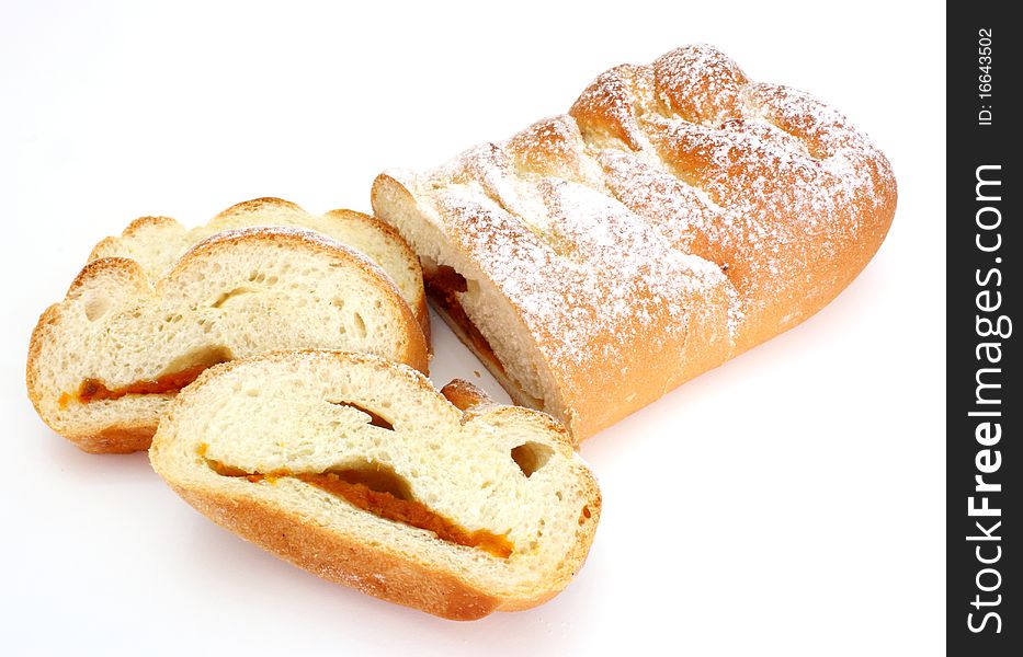 The rich ruddy roll is strewed by powdered sugar with a stuffing from dried apricots on a white background. The rich ruddy roll is strewed by powdered sugar with a stuffing from dried apricots on a white background