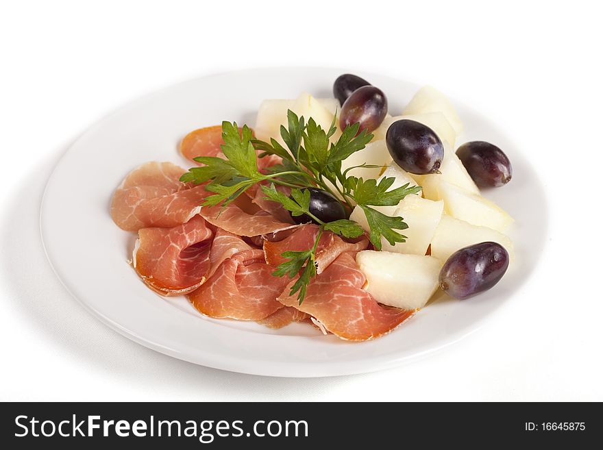 Smoked meat beef slices with melon cubes and grapes on ceramic plate