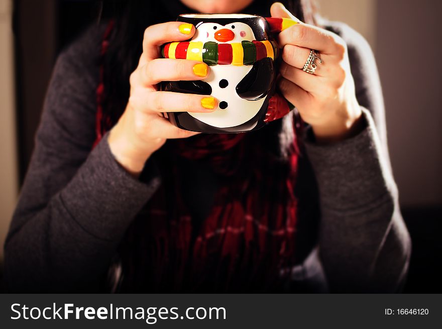 Girl drinking hot cocoa out of a penguin cup wrapped up in a red scarf.