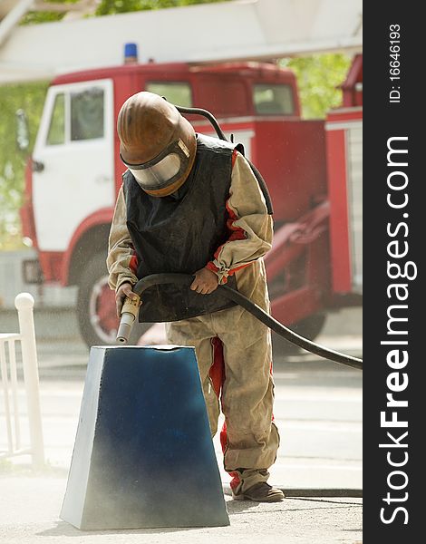 Worker in a protective suit spraying sand  with abrasive peeler