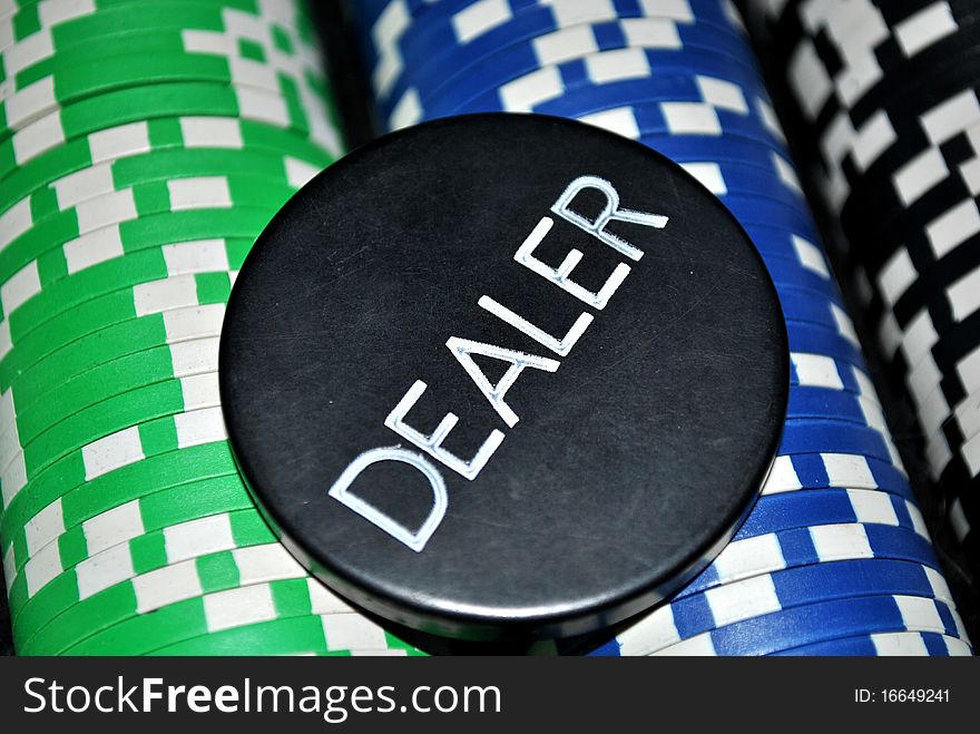 Playing cards and poker chips with focus on dealer chip.