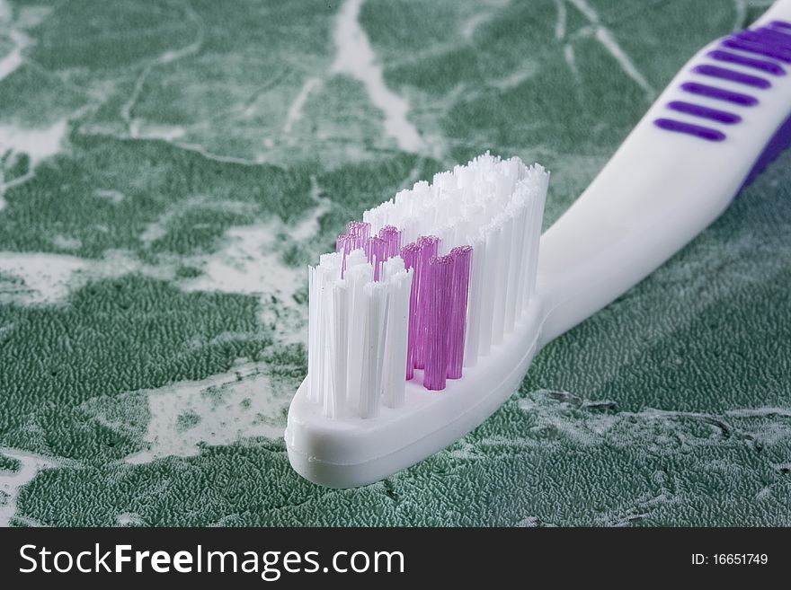 White and purple toothbrush on the green countertop.