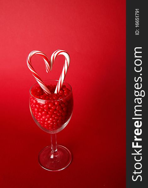 Heart made out of candy canes in a goblet filled with red hot candies on a red background. Heart made out of candy canes in a goblet filled with red hot candies on a red background