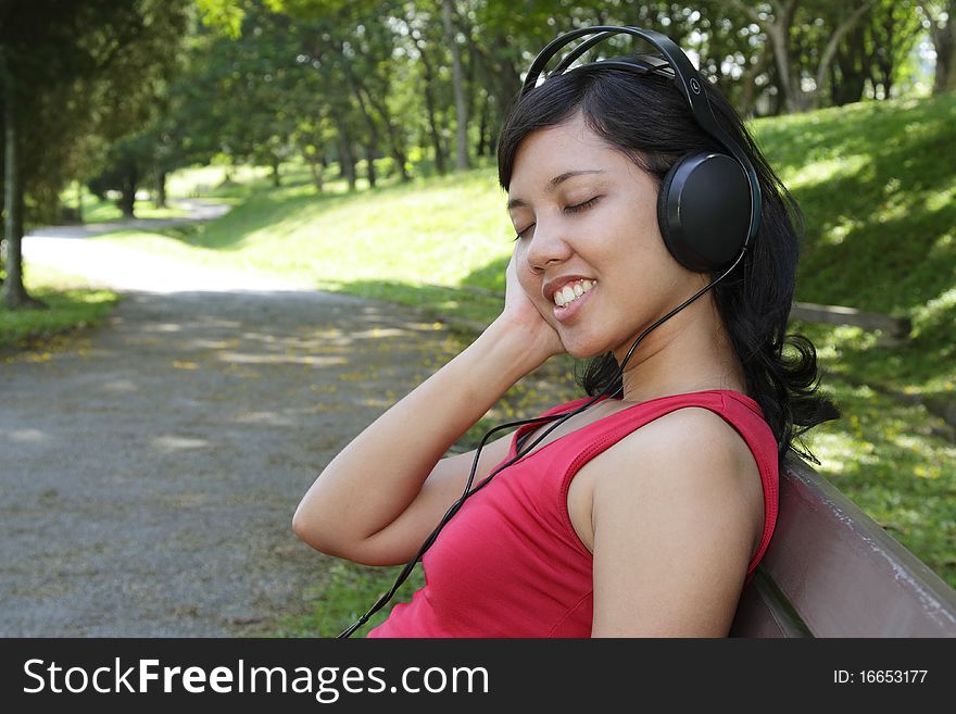 An Asian woman listening to music at a park