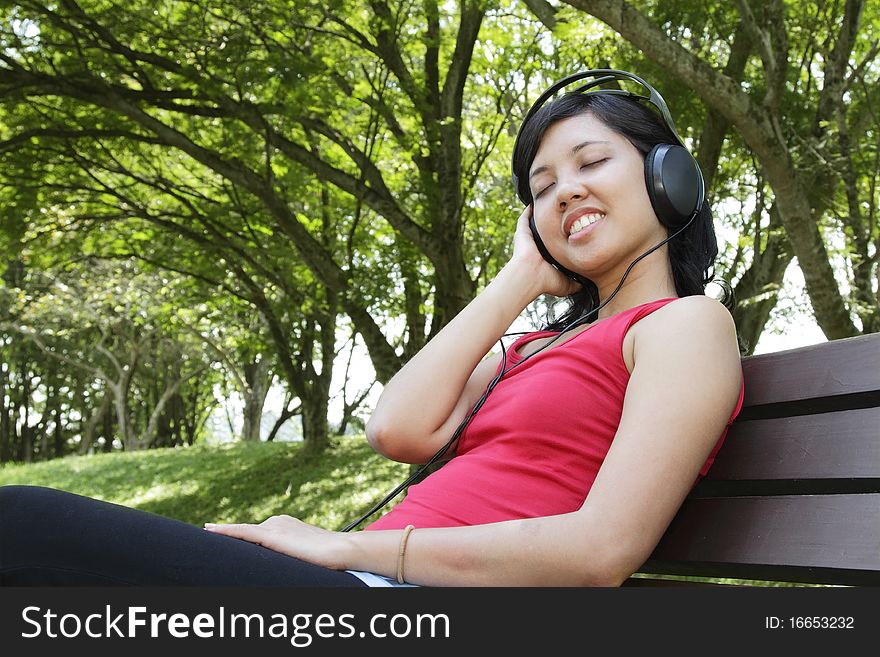 An Asian woman listening to music at a park