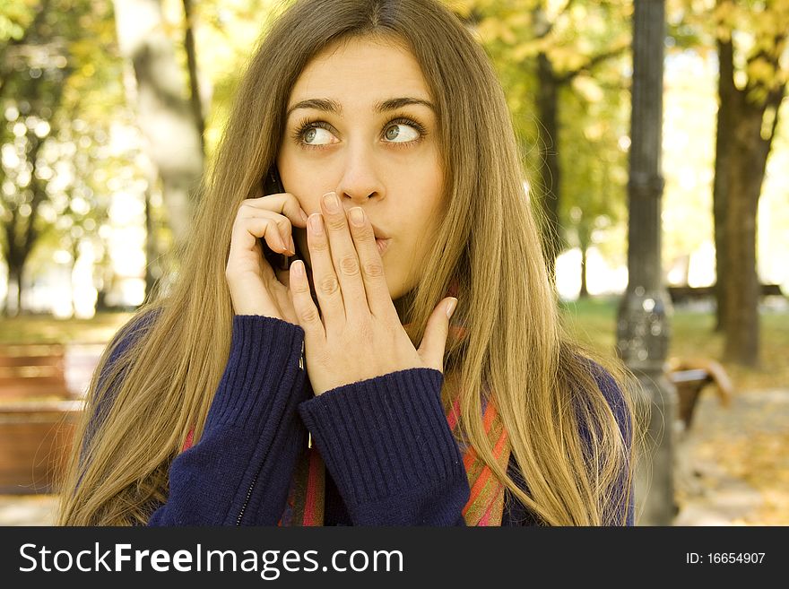 Autumn portrait of a beautiful girl outside on the phone shocking news. Autumn portrait of a beautiful girl outside on the phone shocking news