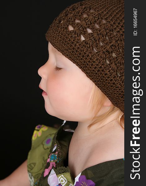 Cute little girl wearing a brown knitted hat sitting with eyes closed. Cute little girl wearing a brown knitted hat sitting with eyes closed