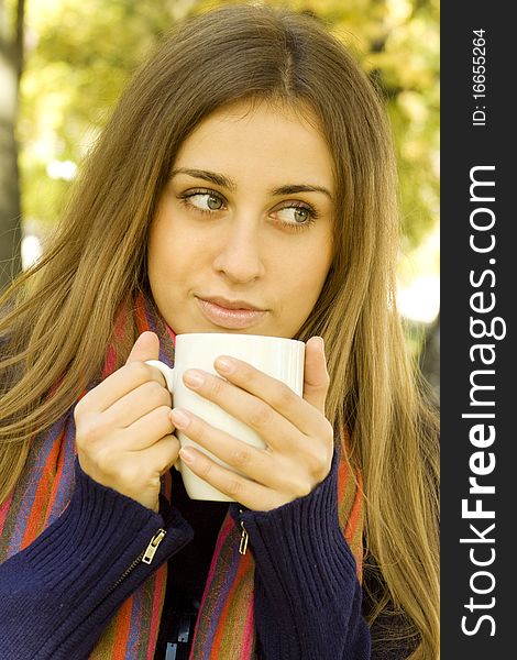 Autumn portrait of an attractive young woman wearing a soft sweater and scarf, holding a cup coffee (or tea). Autumn portrait of an attractive young woman wearing a soft sweater and scarf, holding a cup coffee (or tea)