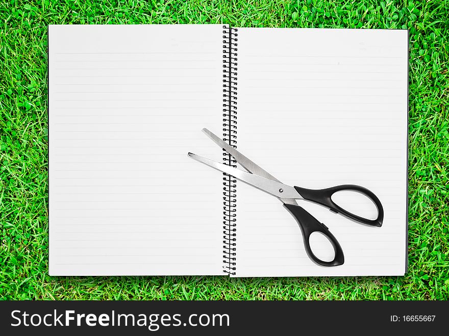 Blank notebook open two page with scisscors on green grass field. Blank notebook open two page with scisscors on green grass field