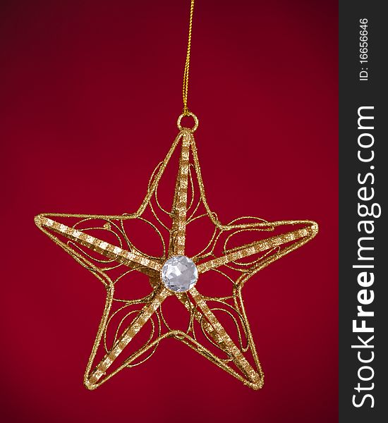 A gold Christmas tree star ornament isolated against a red background. A gold Christmas tree star ornament isolated against a red background.