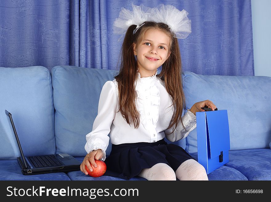 Schoolgirl girl with laptop, backpack and red apple in sofa