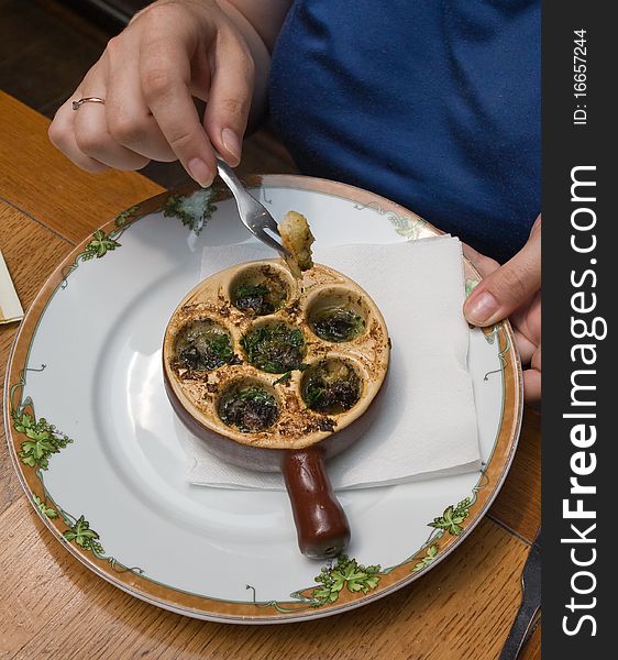 Plate with baked snail, piece of bread with a fork, dip it in the oil