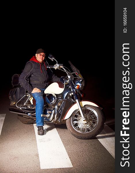 Lonely rider sitting on custom motorcycle in the middle of night street.