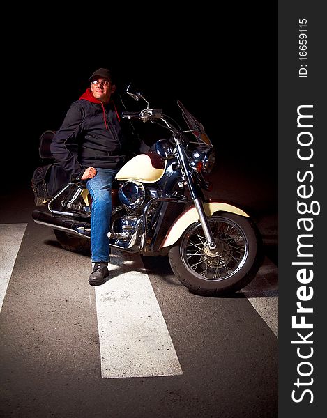 Lonely rider sitting on custom motorcycle in the middle of night street.