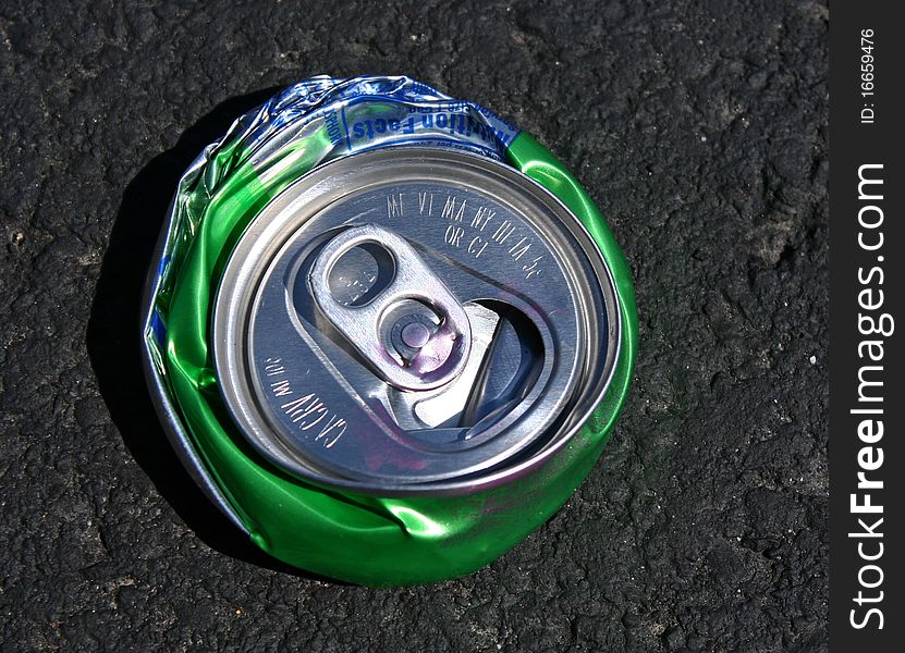 Top view of a crushed circular, green, aluminum soda can with pop top and some pink lipstick stain. Top view of a crushed circular, green, aluminum soda can with pop top and some pink lipstick stain