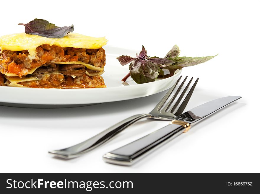 Lasagna on the white plate decorated with basil near to knife and fork. Lasagna on the white plate decorated with basil near to knife and fork