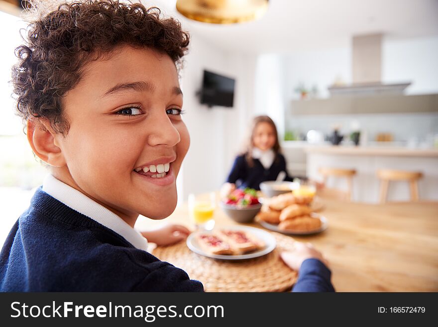 Portrait Of Children Wearing Uniform In Kitchen Eating Breakfast Before Going To School