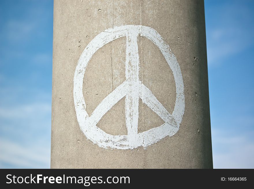 Peace sign on a concrete pillar with blue sky and clouds.