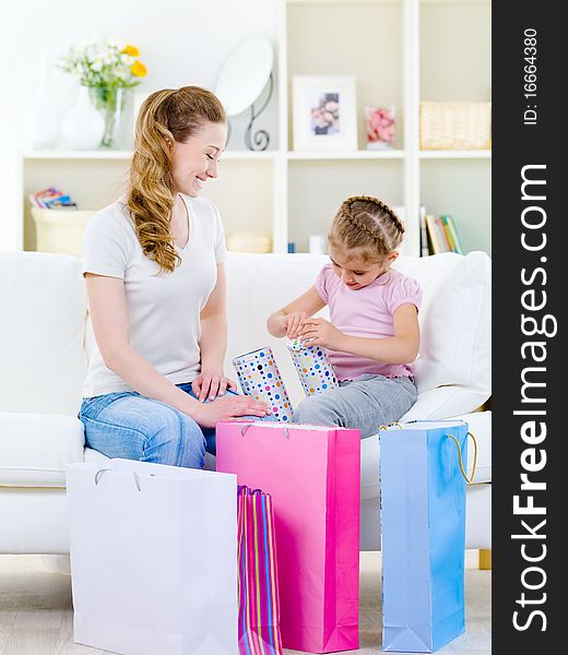 Mother looking at her little daughter openning gift - at home. Mother looking at her little daughter openning gift - at home