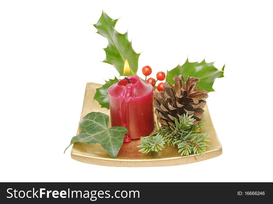 Christmas table decoration of holly, ivy, pine needles and a pine cone with a burning red candle on a gold dish