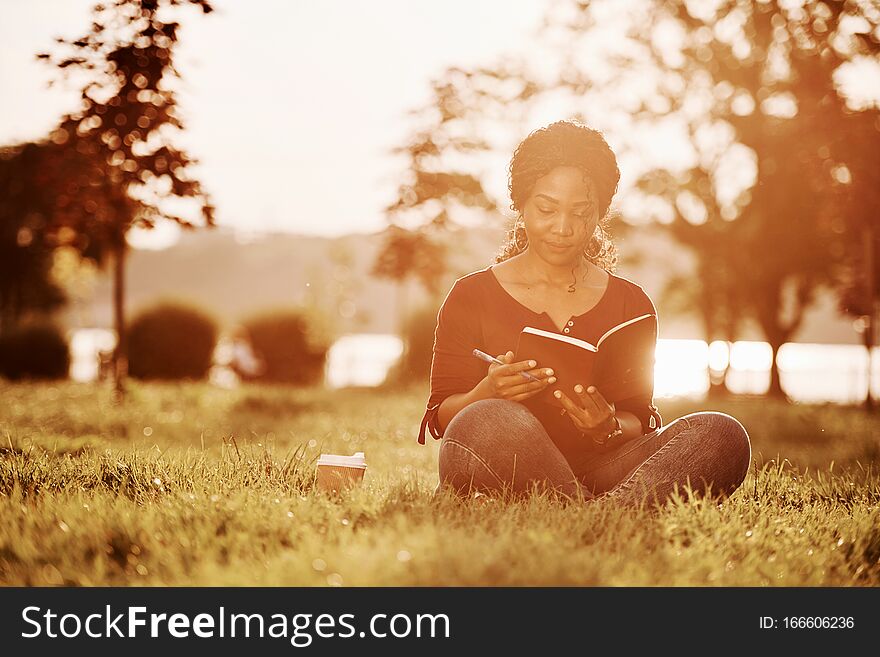 Education process. Cheerful african american woman in the park at summertime.