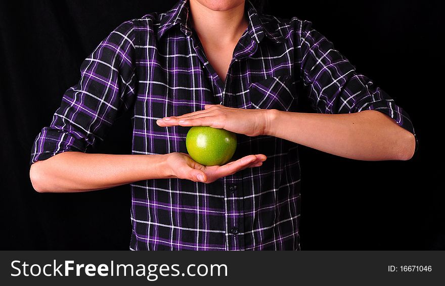 A girl holding a green apple with her two arms, on a black background. A girl holding a green apple with her two arms, on a black background