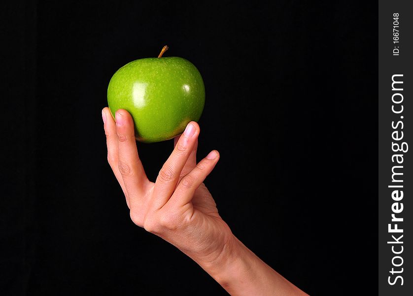 A female hand holding in exhibition a green apple on a black background. A female hand holding in exhibition a green apple on a black background