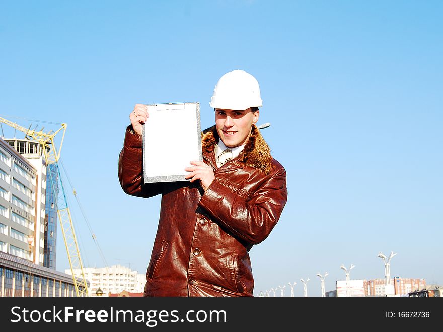 Industrial theme: architect, on a workplace, in a warm winter jacket and a helmet, has control over a tablet. Industrial theme: architect, on a workplace, in a warm winter jacket and a helmet, has control over a tablet.