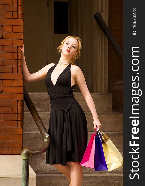 Beautiful blond woman leaning on the wall with shopping bags in her hand. Beautiful blond woman leaning on the wall with shopping bags in her hand