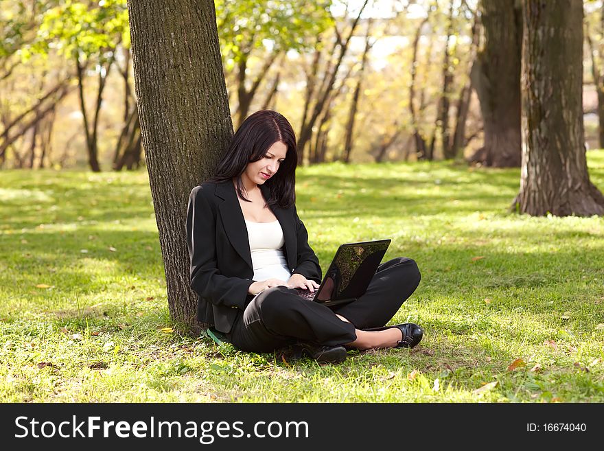 Young businesswoman sitting on the grass and  working with laptop