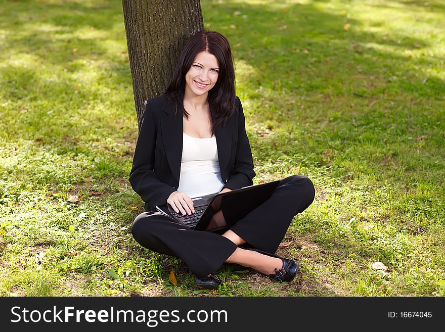 Young businesswoman sitting on the grass and  working with laptop