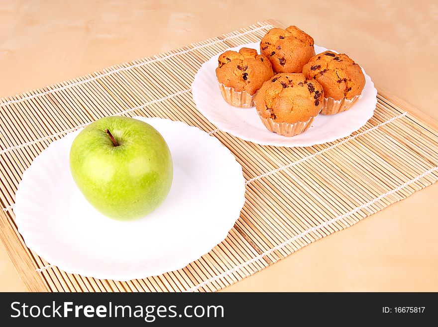 Apple and cakes on white plates, closed-up on wooden pad