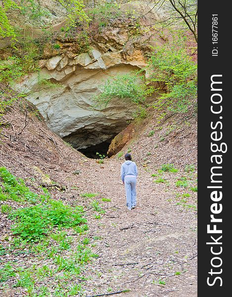 Young woman approaching the entrance of an mountain cave, having doubts about entering or not. Young woman approaching the entrance of an mountain cave, having doubts about entering or not