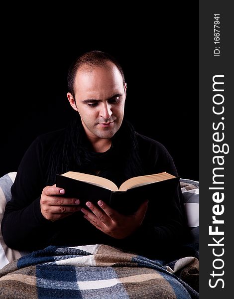 Man lying on the couch reading a book, isolated on black, studio shot.
