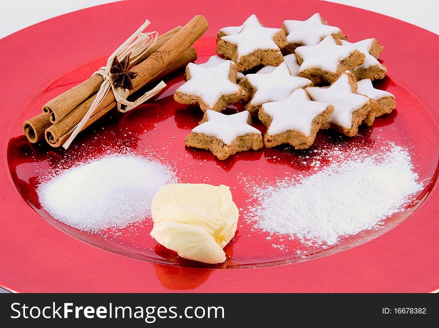 Red plate with star-shaped cinnamon biscuits and baking ingredients. Red plate with star-shaped cinnamon biscuits and baking ingredients
