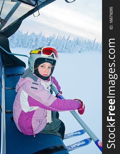 Little girl-skier on the ski lift watching the sunrise at a ski resort in Finland