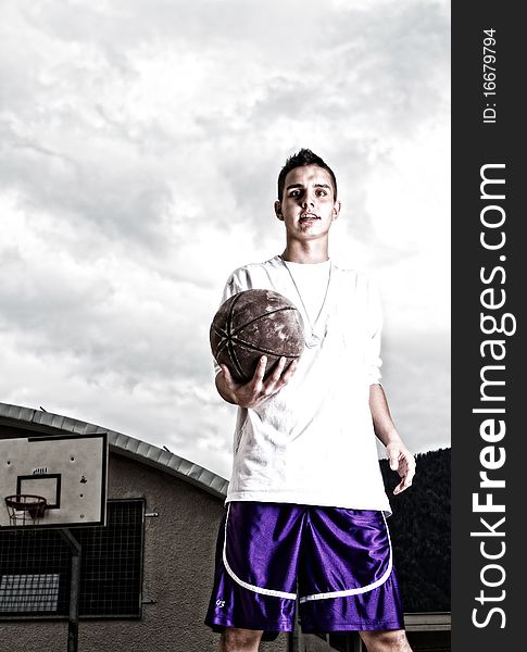 Young stylish teenage basketball player on the street with dark clouds over him. Young stylish teenage basketball player on the street with dark clouds over him.